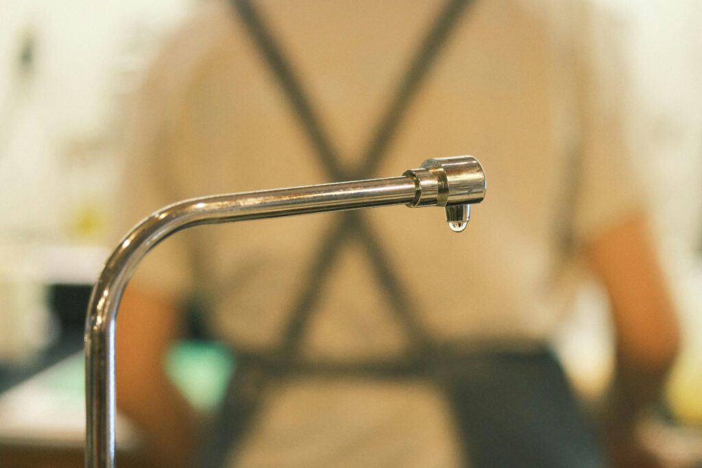 A focused shot of a metal faucet with a single drip indoors, capturing water conservation.